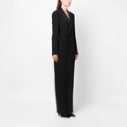 Side full-length studio shot of a model wearing a black double-breasted tuxedo maxi dress.