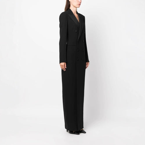 Side full-length studio shot of a model wearing a black double-breasted tuxedo maxi dress.