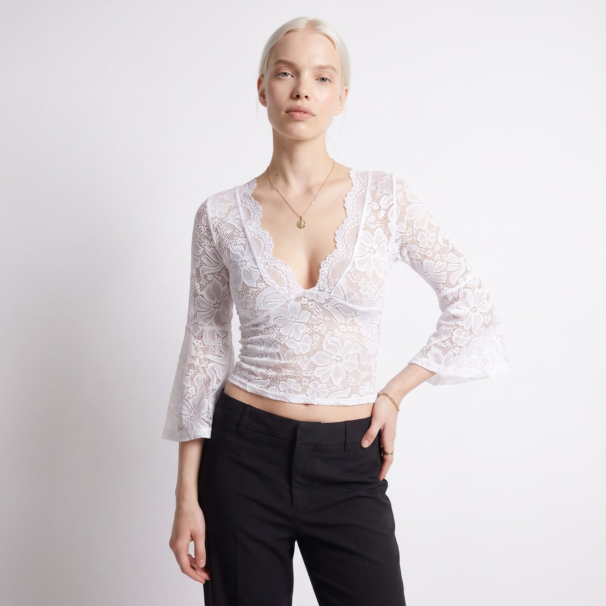 Front view of a woman wearing a white floral lace crop top with bell sleeves and black trousers.