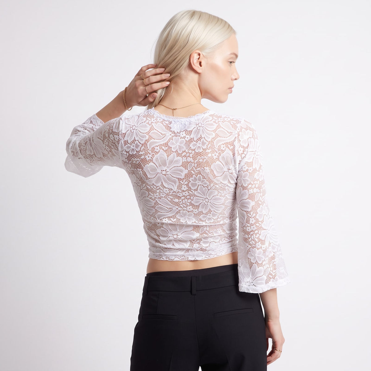 Back view of a woman wearing a white floral lace crop top with bell sleeves.