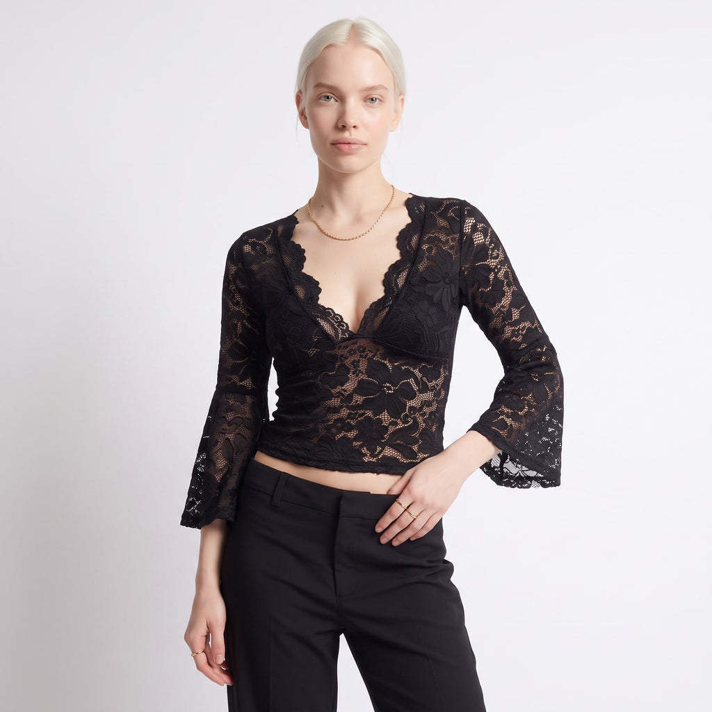 Front view of a woman wearing a black floral lace crop top with bell sleeves and black trousers.