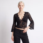 Front view of a woman wearing a black floral lace crop top with bell sleeves and black trousers.