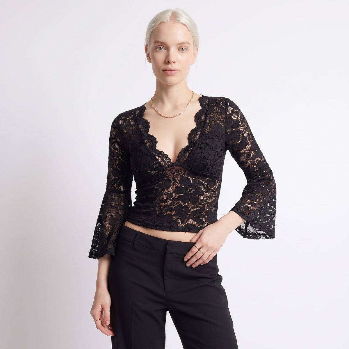 Front view of a woman wearing a black floral lace crop top with bell sleeves and black trousers.