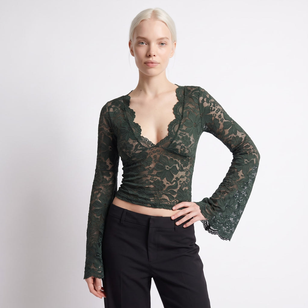 Front view of a woman wearing a dark green floral lace crop top with bell sleeves and black trousers.