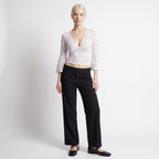Full body front view of a woman wearing a white floral lace crop top and black wide-leg trousers.