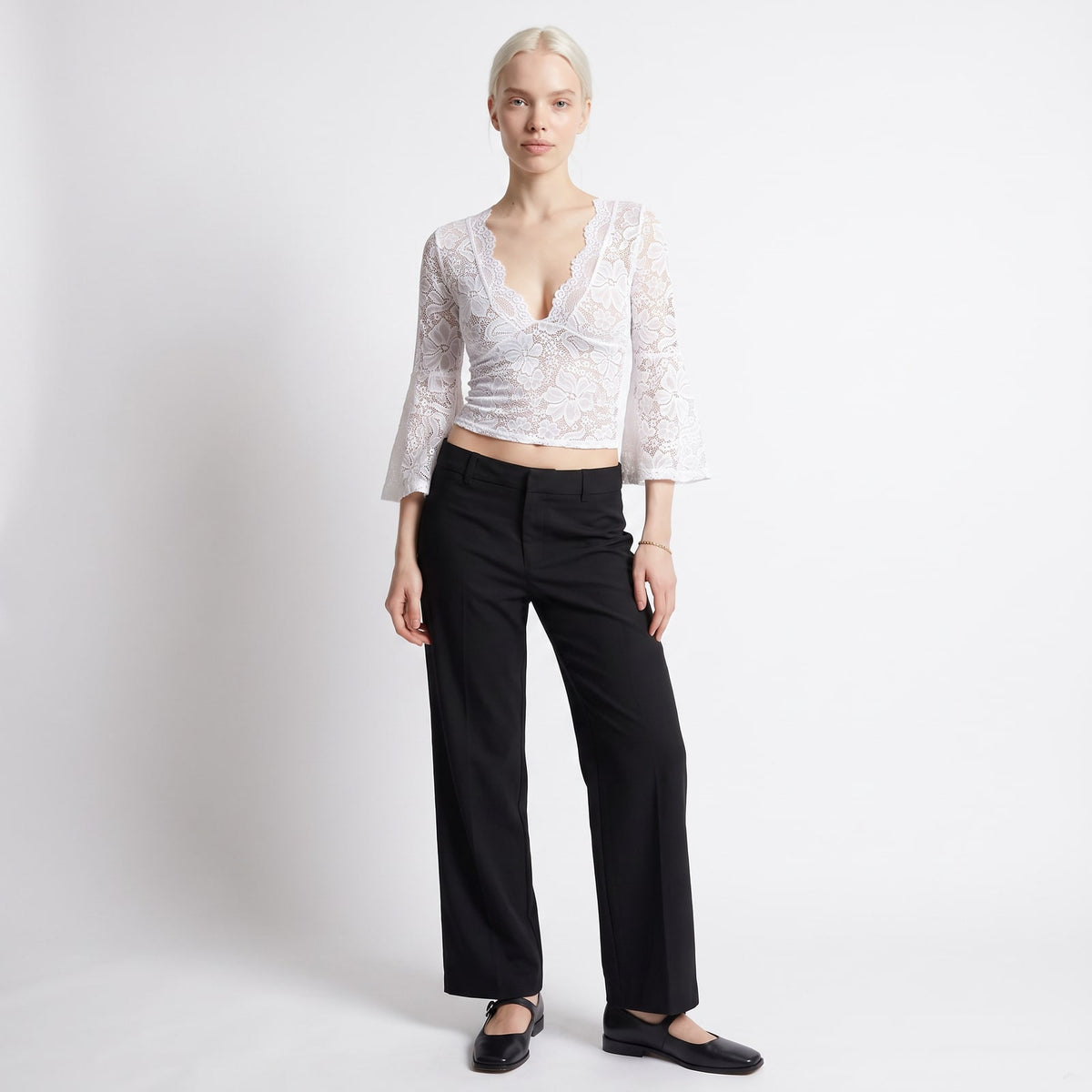 Full body front view of a woman wearing a white floral lace crop top and black wide-leg trousers.