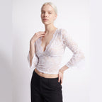 Front view of a woman posing in a white floral lace crop top with bell sleeves.