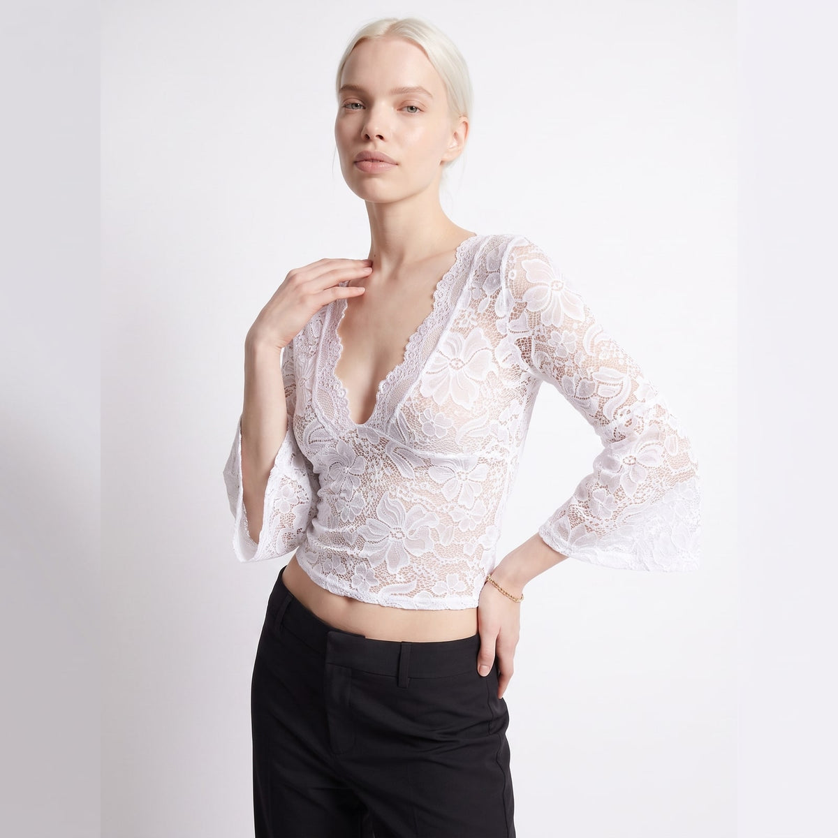 Front view of a woman posing in a white floral lace crop top with bell sleeves.