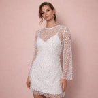 Front view of a woman modeling a white sequined mini-dress with sheer long sleeves against a pink background.