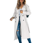 Front view of a woman wearing a white longline double-breasted trench coat over a white top and ripped blue jeans.