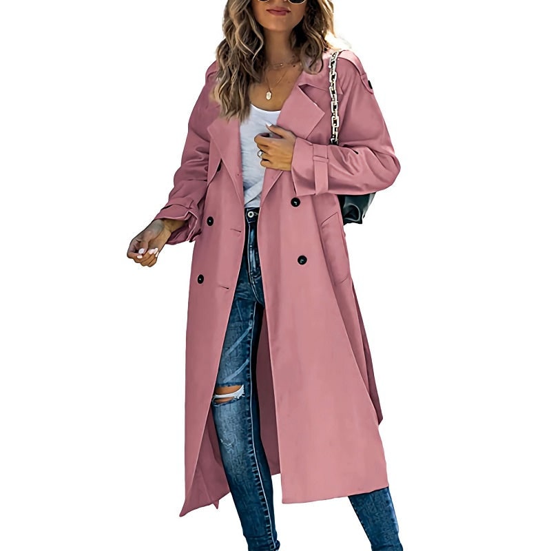 Front view of a woman wearing a pink longline double-breasted trench coat over a white top and ripped blue jeans.