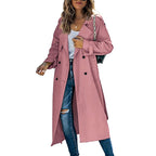 Front view of a woman wearing a pink longline double-breasted trench coat over a white top and ripped blue jeans.