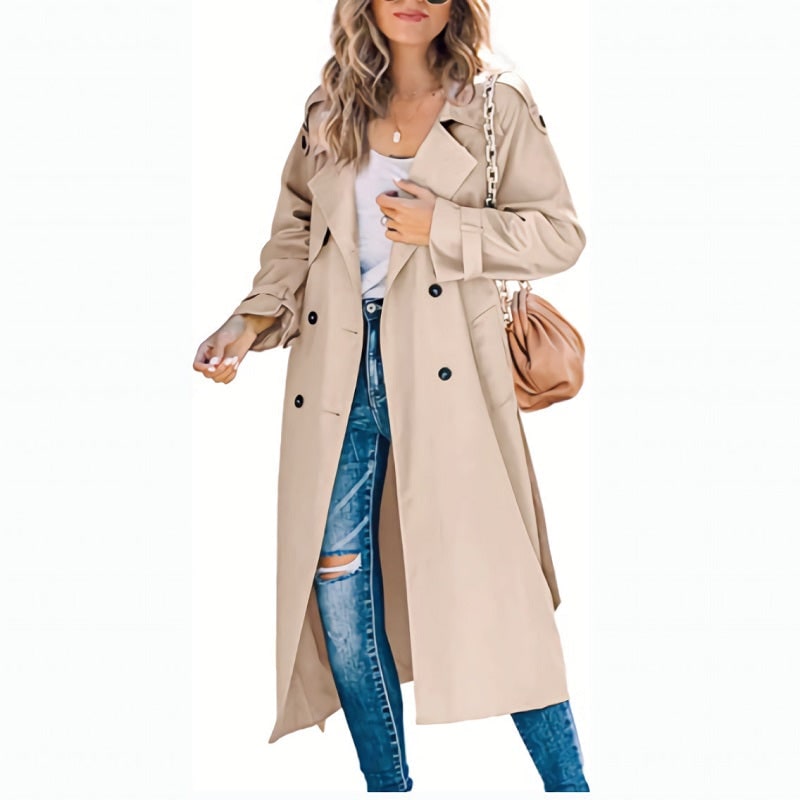 Front view of a woman wearing a beige longline double-breasted trench coat over a white top and ripped blue jeans.