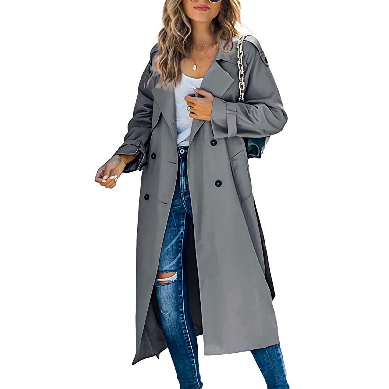 Front view of a woman wearing a grey longline double-breasted trench coat over a white top and ripped blue jeans.