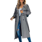 Front view of a woman wearing a grey longline double-breasted trench coat over a white top and ripped blue jeans.