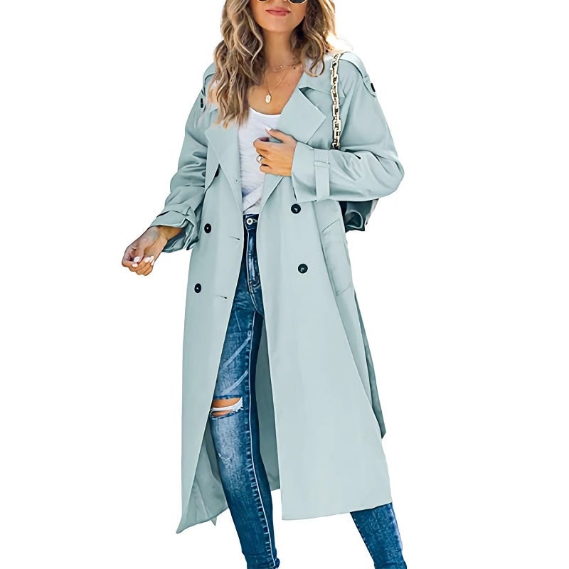 Front view of a woman wearing a light blue longline double-breasted trench coat over a white top and ripped blue jeans.