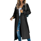 Front view of a woman wearing a black longline double-breasted trench coat over a white top and ripped blue jeans.