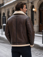 Back view of a man wearing a brown shearling aviator jacket, standing on a snowy street.