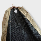 An angled view of the open beige trench coat showing its black quilted lining.