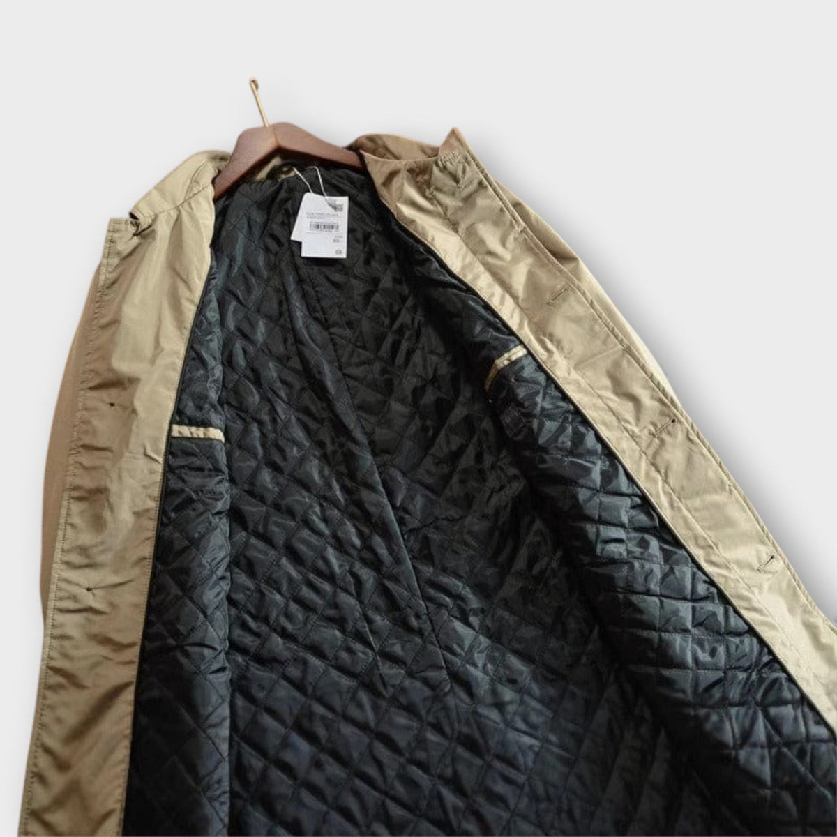 An angled view of the open beige trench coat showing its black quilted lining.