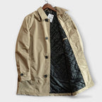A front view of the open beige trench coat displaying its black quilted interior.