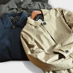 A close-up of three trench coats in beige, navy, and dark grey, stacked together.