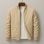 Front view of a beige bomber jacket with brown and white striped ribbed trim, partially unzipped to show a white t-shirt underneath.