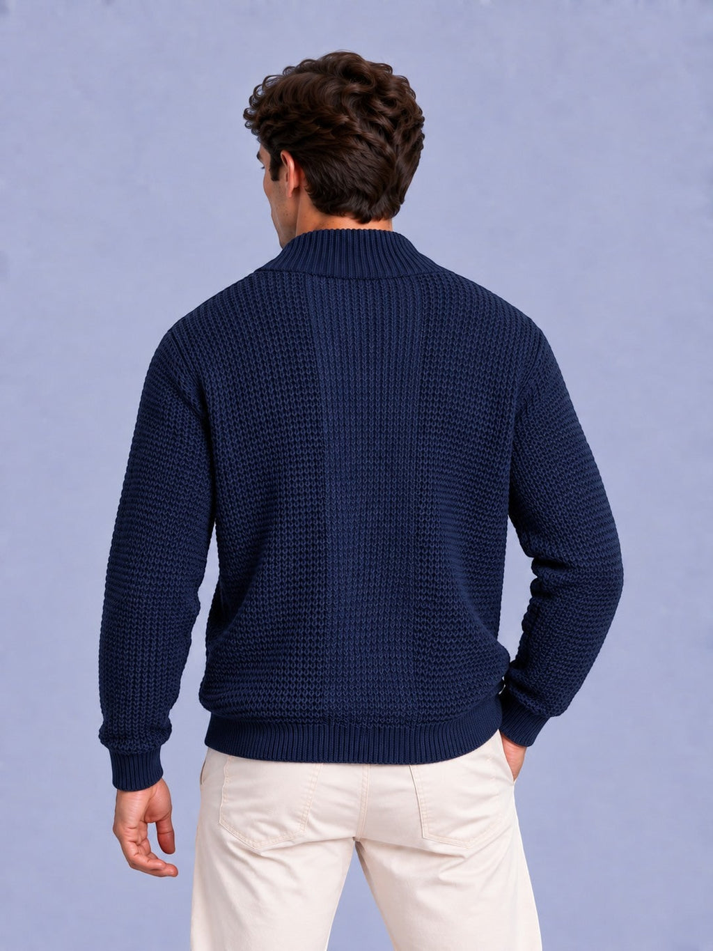 Rear view of a man wearing a navy blue waffle knit zip-up sweater and light-colored pants.
