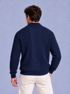 Rear view of a man wearing a navy blue waffle knit zip-up sweater and light-colored pants.