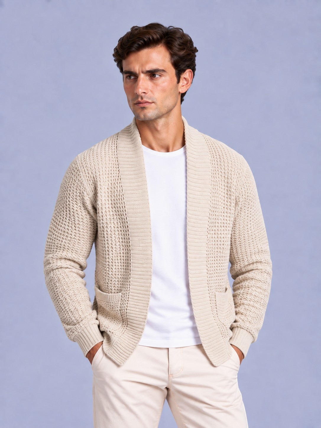 Front view of a man wearing a beige waffle knit open cardigan with pockets over a white t-shirt and light-colored pants.