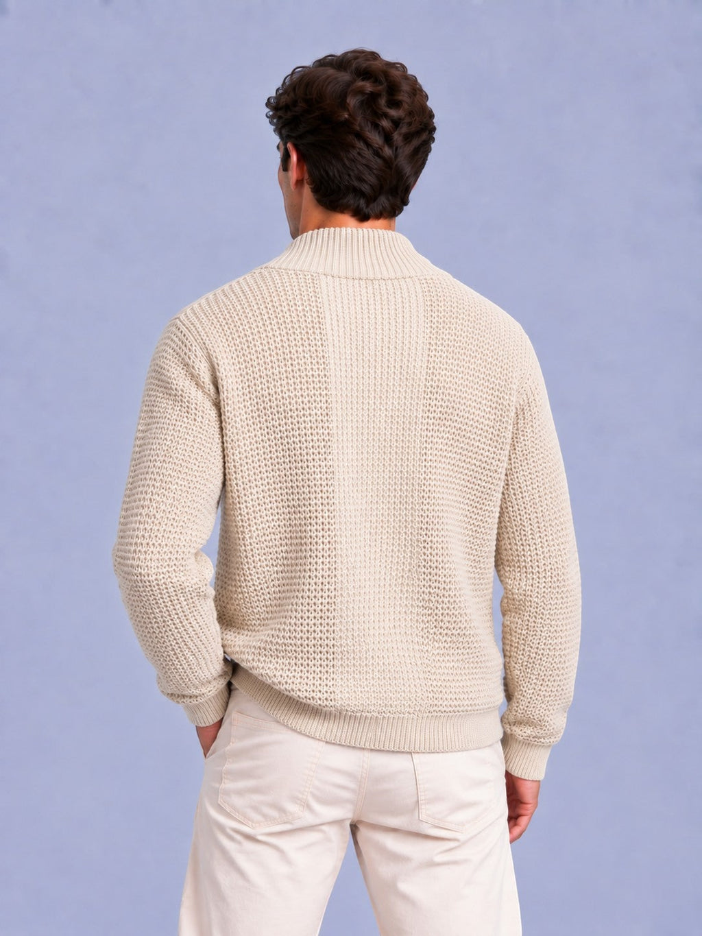 Rear view of a man wearing a beige waffle knit zip-up sweater and light-colored pants.