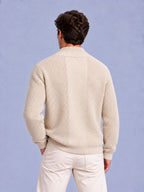Rear view of a man wearing a beige waffle knit zip-up sweater and light-colored pants.