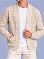 Close-up front view of a man wearing a beige waffle knit open cardigan with pockets over a white t-shirt.