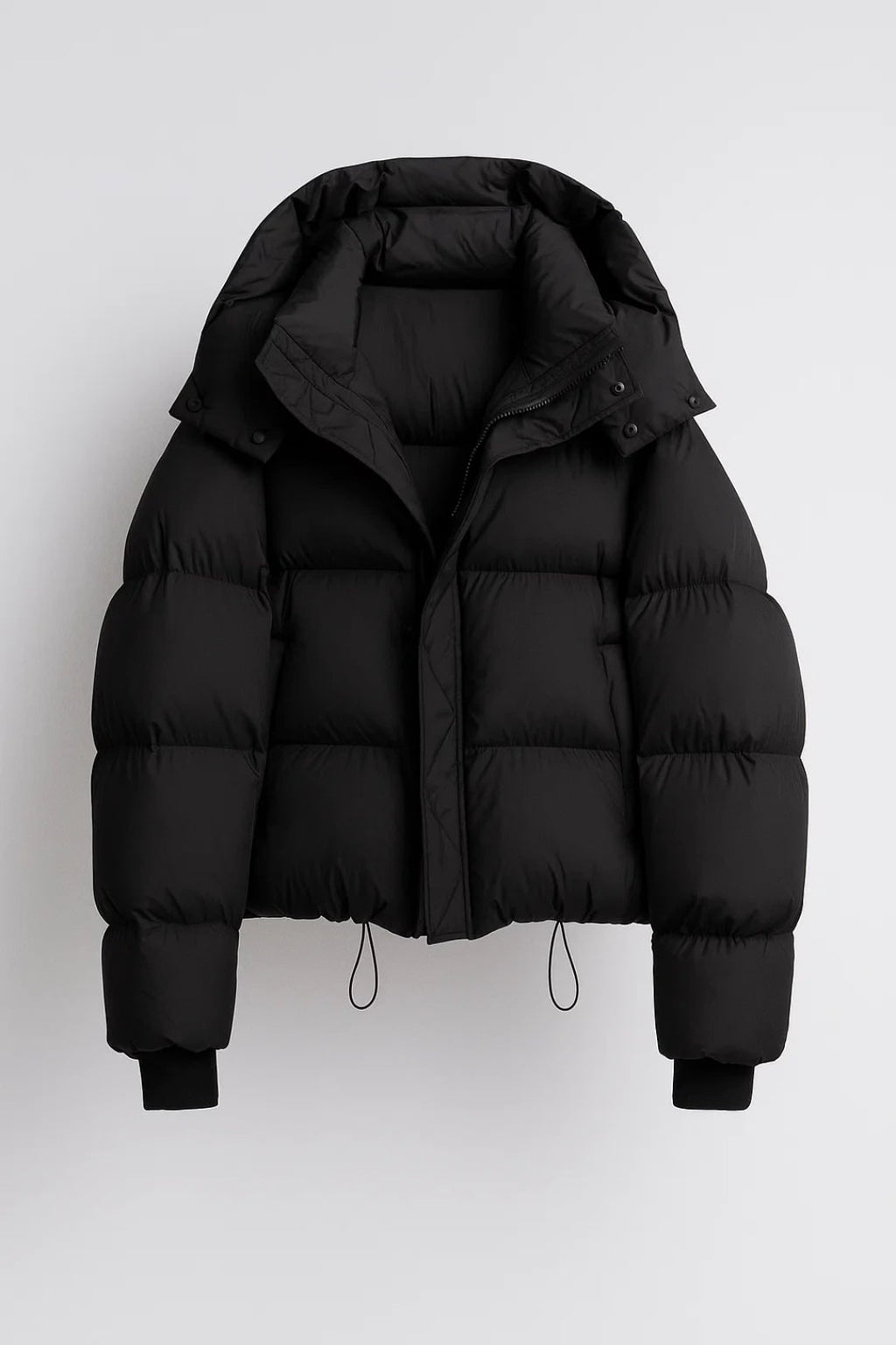 Front view of a black hooded cropped puffer jacket, laid flat on a white background.