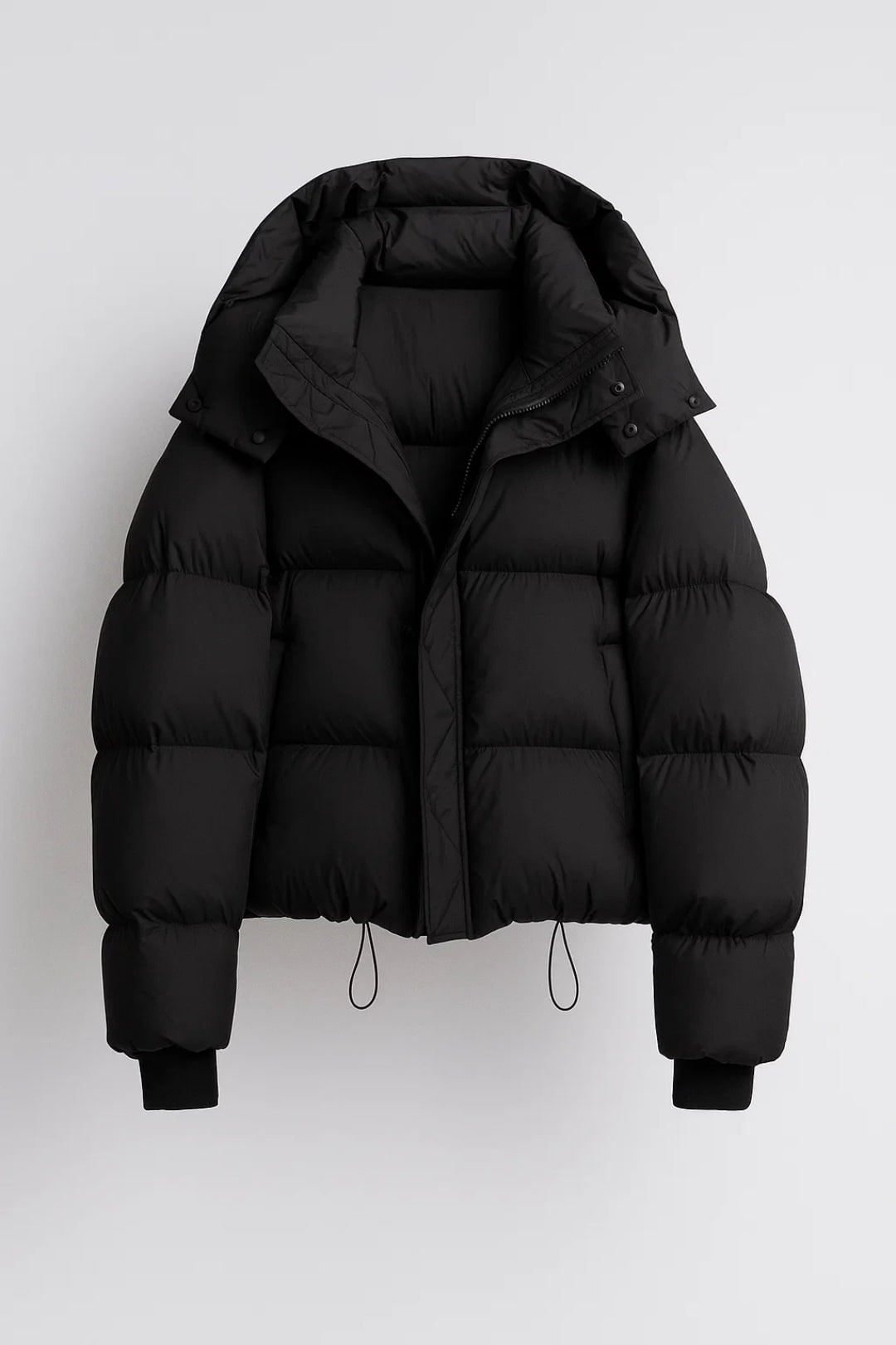 Front view of a black hooded cropped puffer jacket, laid flat on a white background.