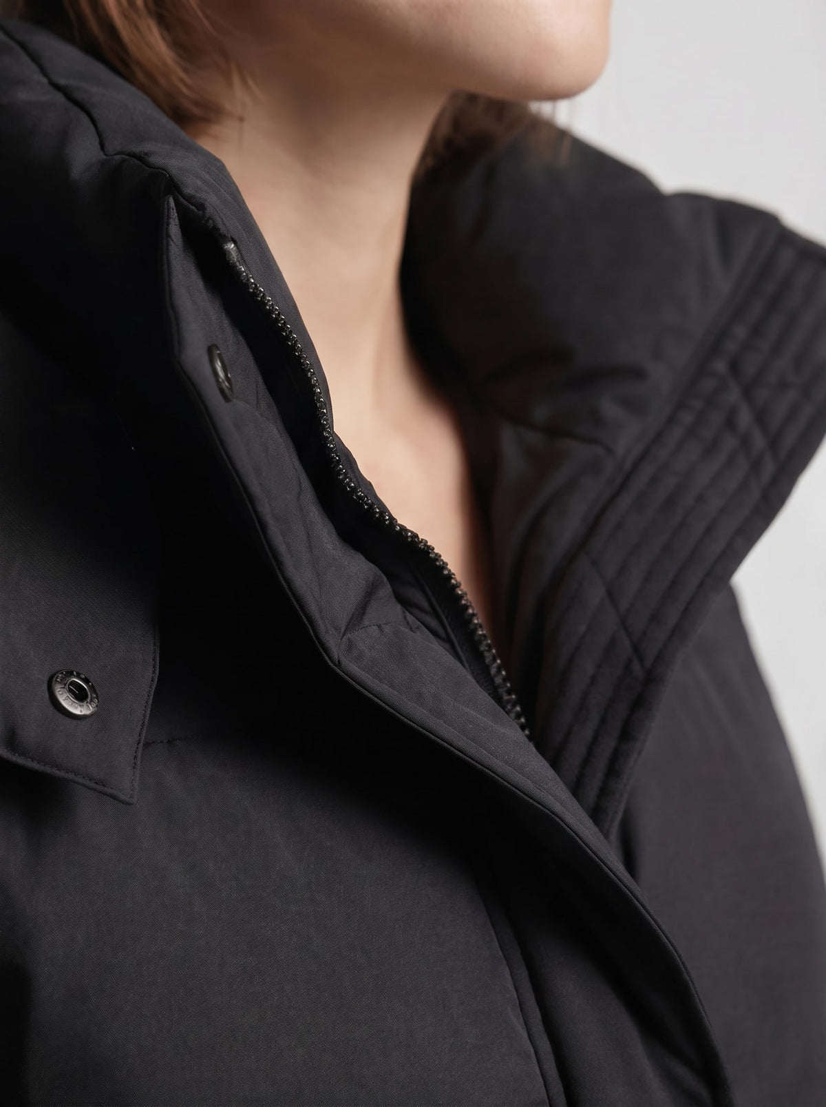 Close-up detail shot of the black puffer jacket's collar, zipper, and snap button closure.