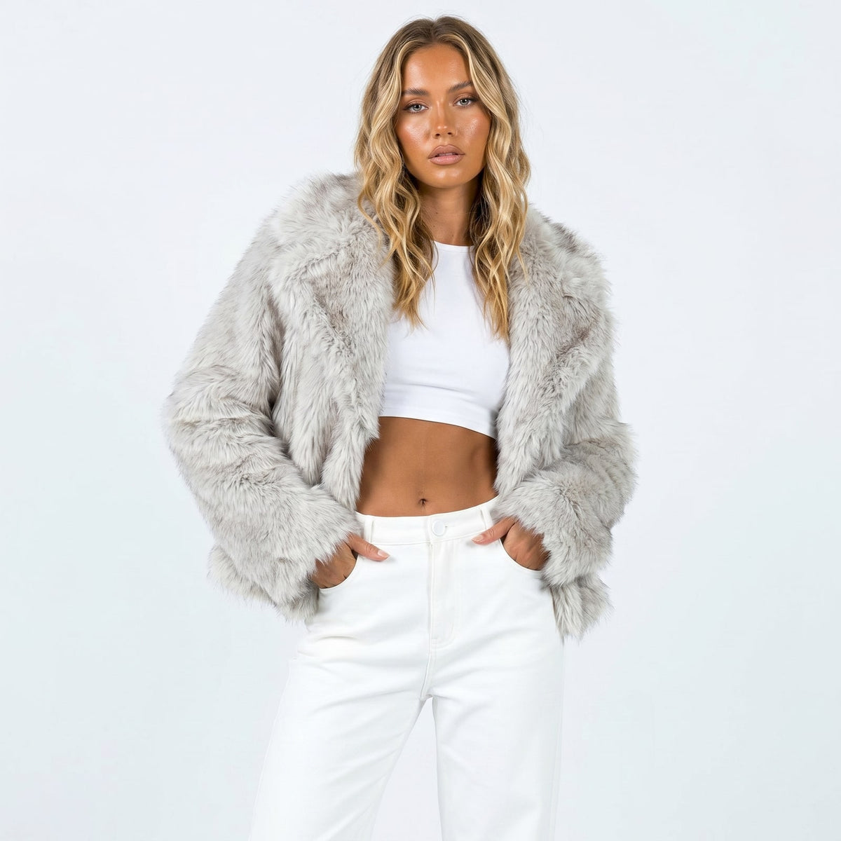 Front view of a woman wearing a light grey faux fur jacket over a white crop top and white pants.