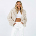 Front view of a woman wearing a cream faux fur jacket over a white crop top and white pants.