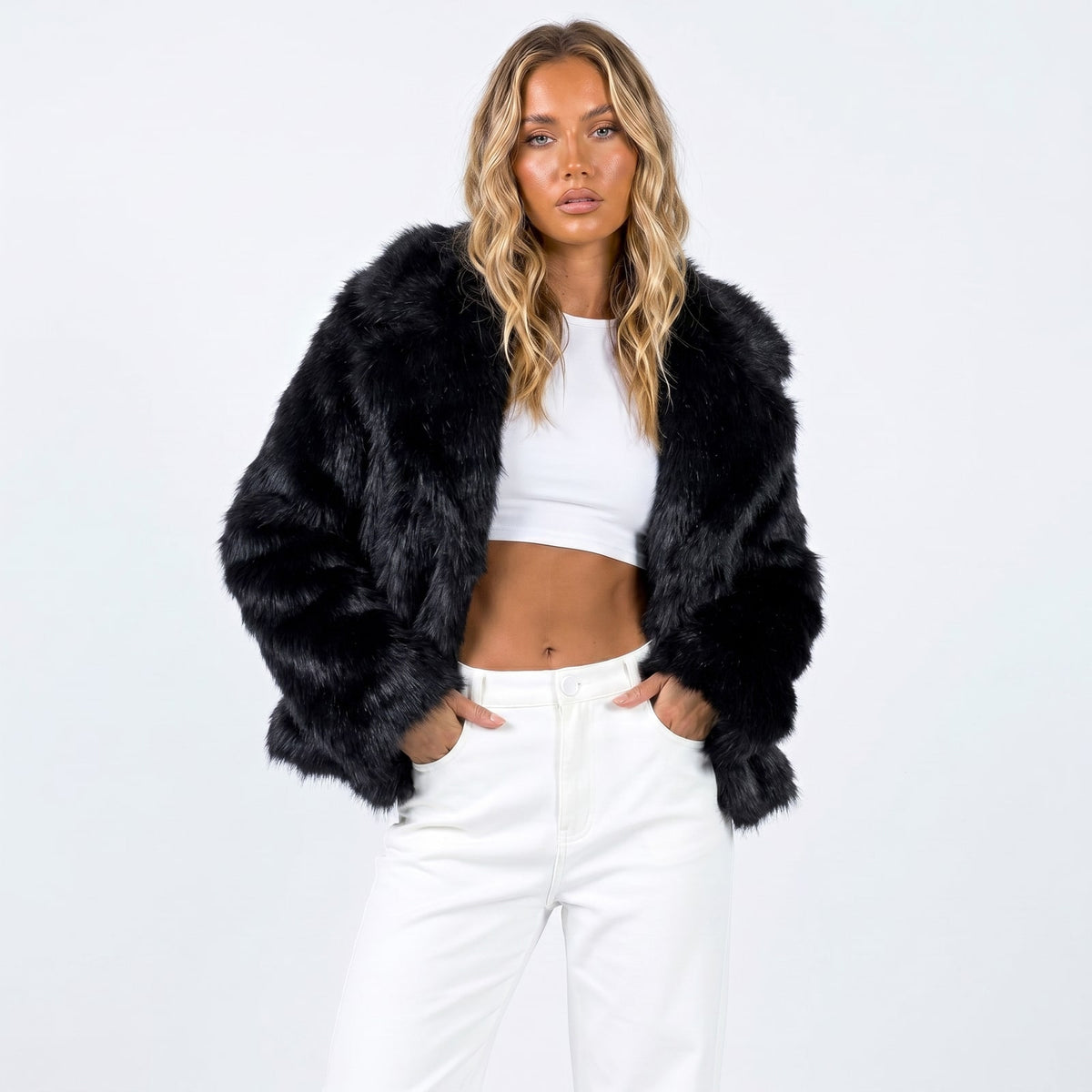 Front view of a woman wearing a black faux fur jacket over a white crop top and white pants.