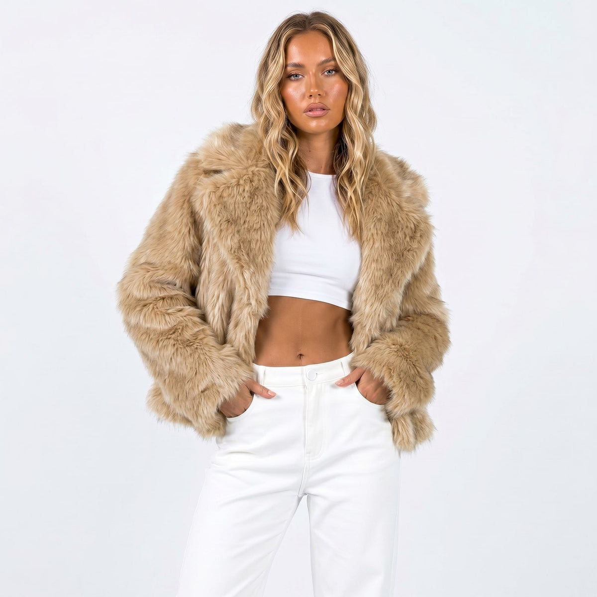 Front view of a woman wearing a tan faux fur jacket over a white crop top and white pants.
