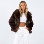 Front view of a woman wearing a brown faux fur jacket over a white crop top and white pants.