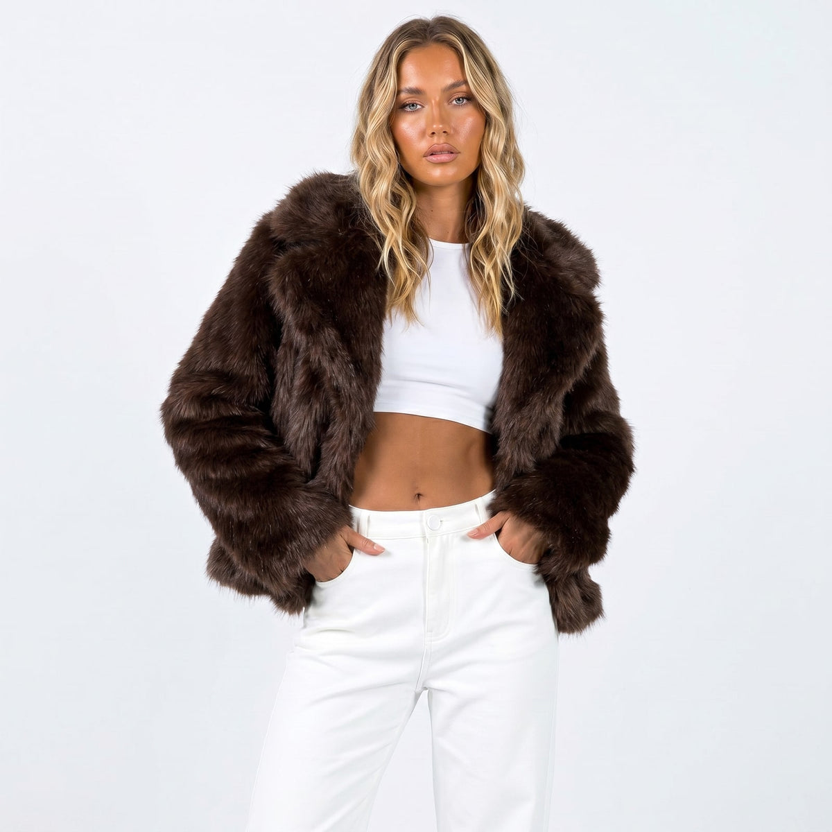 Front view of a woman wearing a brown faux fur jacket over a white crop top and white pants.