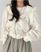 Front view of a model wearing a white cropped oversized zip-up hoodie over a white t-shirt and grey sweatpants.