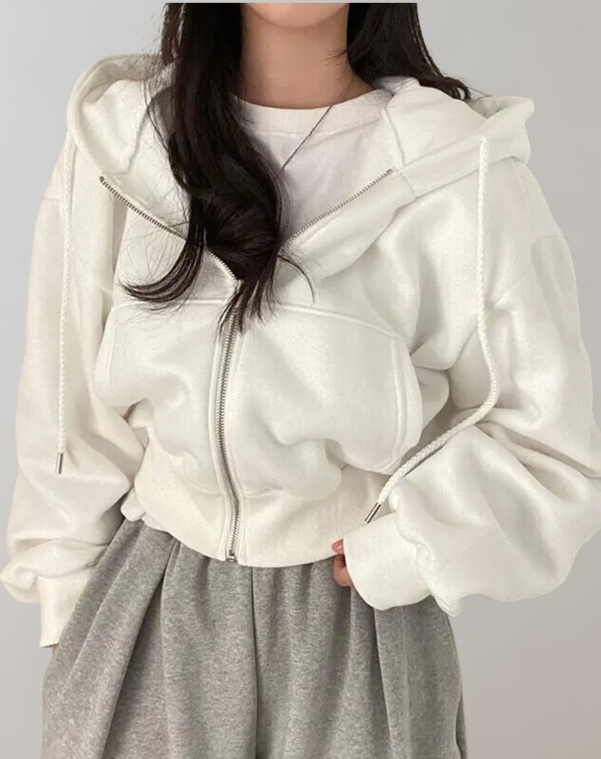 Front view of a model wearing a white cropped oversized zip-up hoodie over a white t-shirt and grey sweatpants.