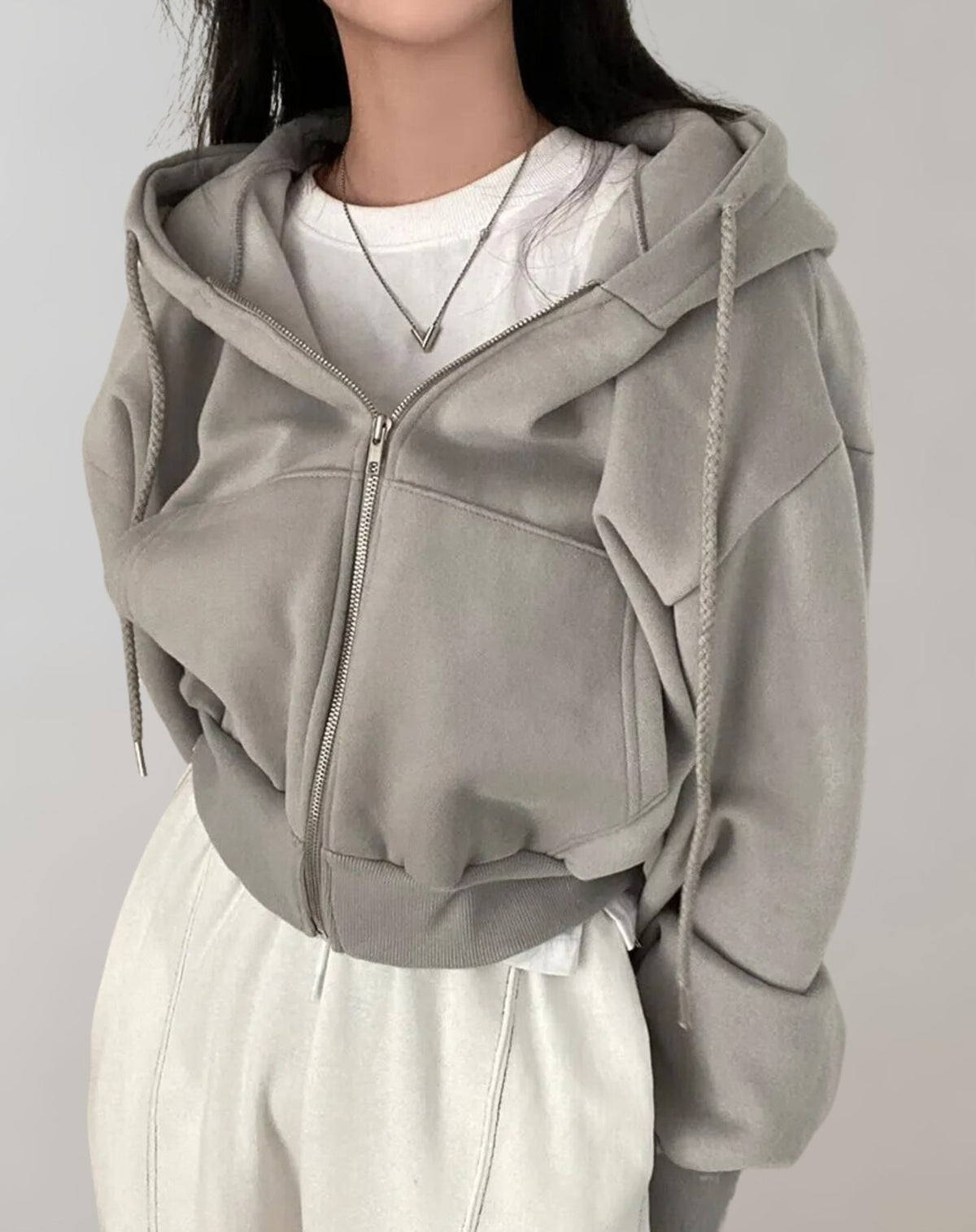 Front view of a model wearing a grey cropped oversized zip-up hoodie over a white t-shirt and white sweatpants.