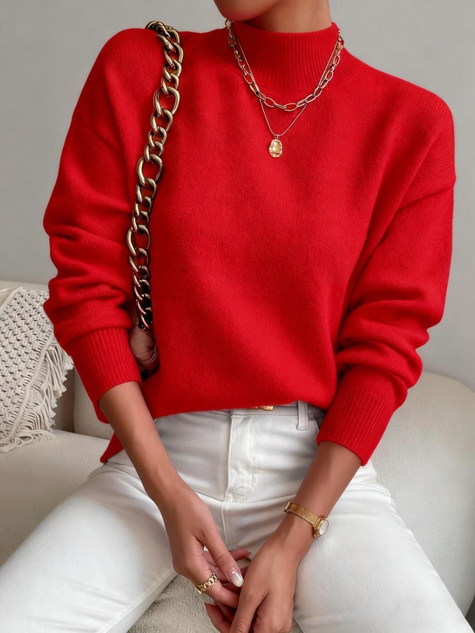 Front view of a woman wearing a red mock neck sweater with white pants, accessorized with a gold necklace, watch, and a gold chain strap bag.
