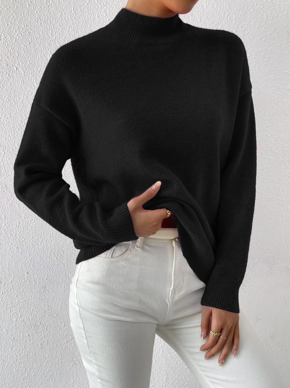 A model wears a black mock-neck sweater and white jeans, with her hand slightly pulling up the sweater to show the fit.