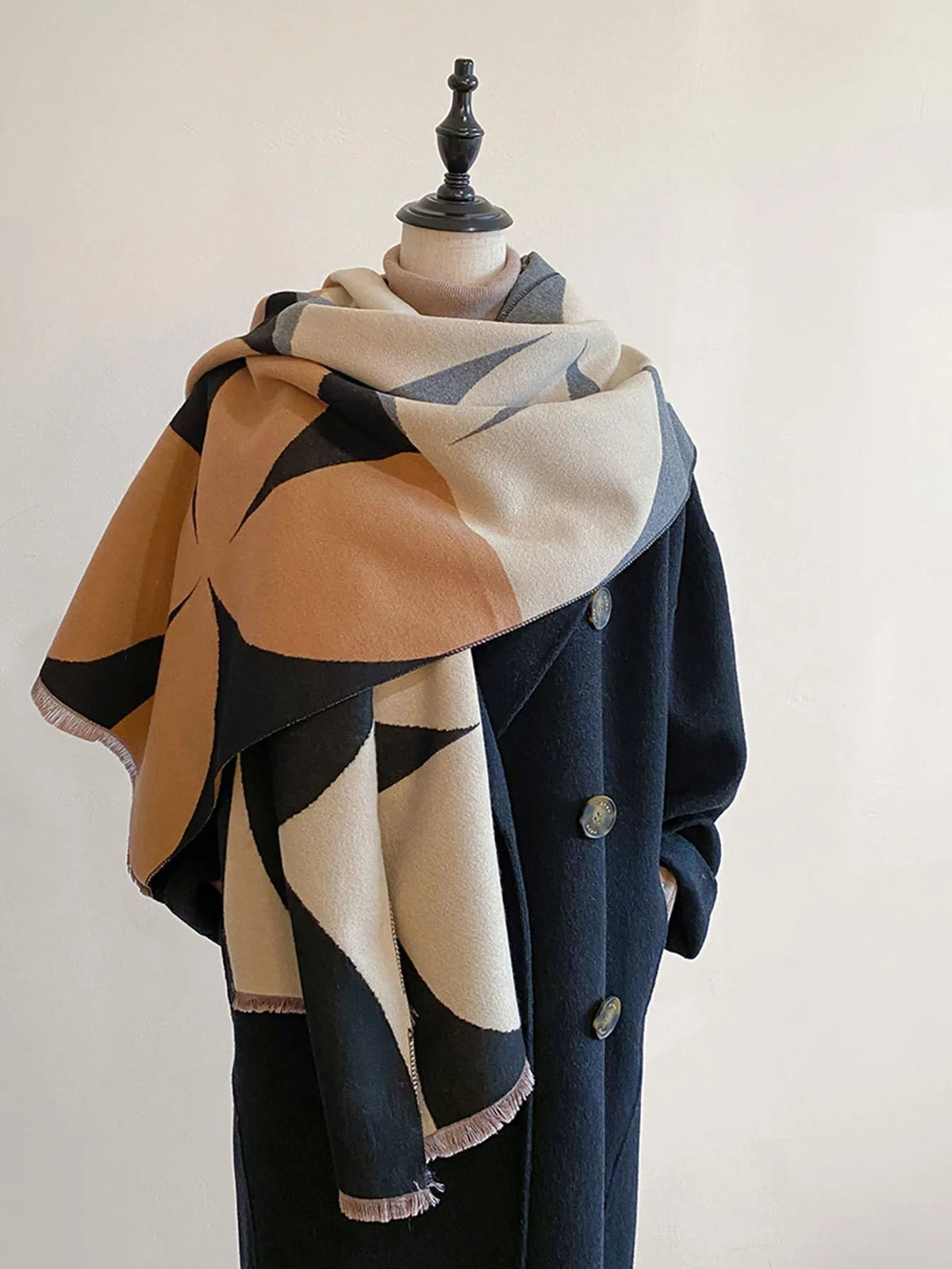 Front view of a black, brown, cream, and grey geometric pattern blanket scarf draped on a mannequin wearing a dark coat.