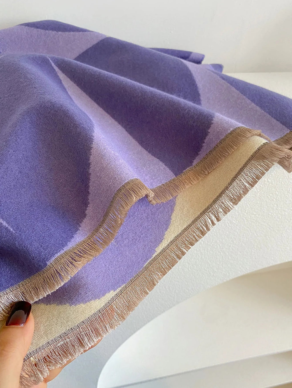 A close-up shot of a purple and cream geometric patterned scarf with fringed edges, held by a hand.