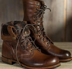 A pair of brown leather lace-up boots, one with the shaft folded down to reveal a fur lining, on a wooden surface.